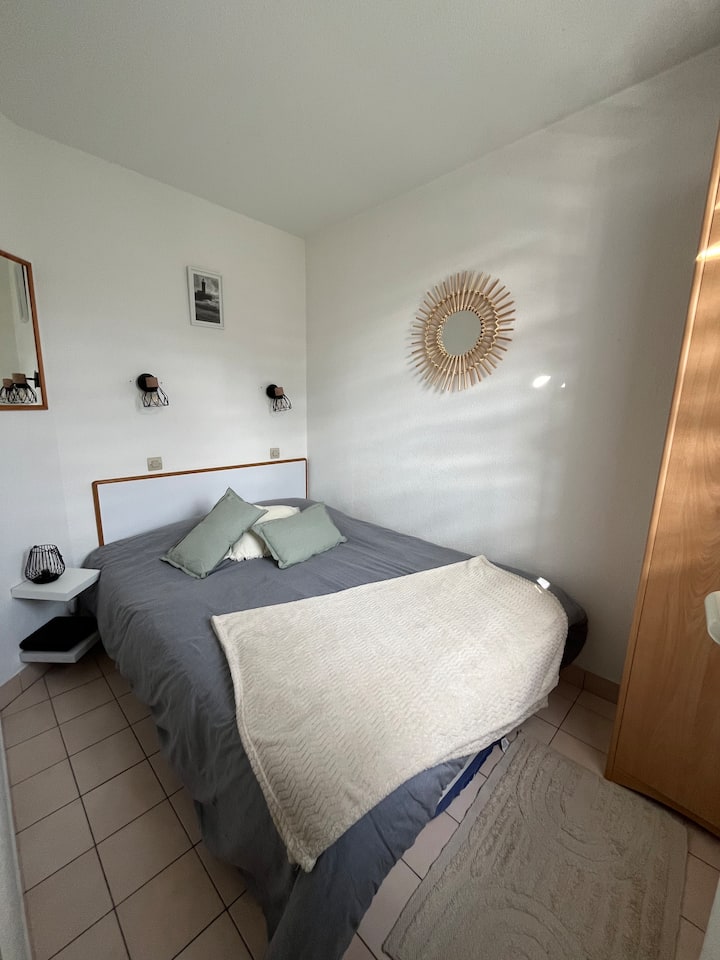 
Habitación con una cama grande, una ventana con persianas y cortinas opacas, sábana bajera, edredón y funda de edredón, fundas de almohada, cojines, armario y estantes con lámpara.
