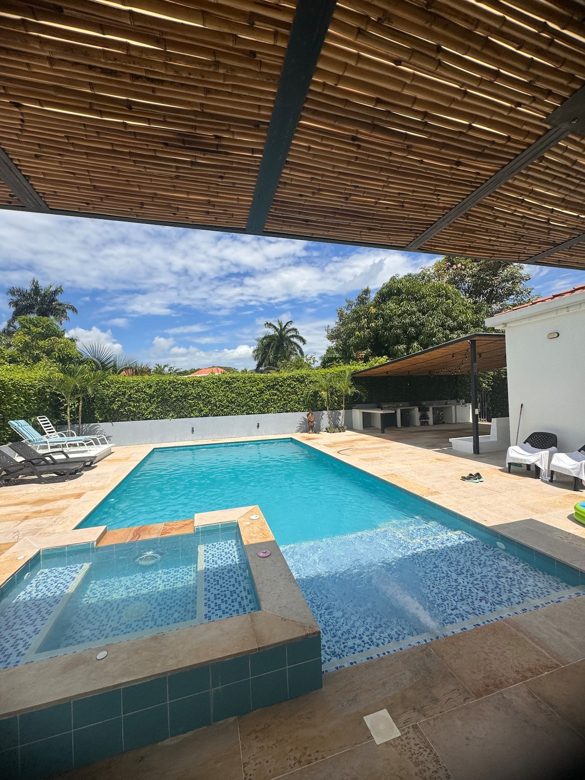 A private swimming pool is framed by a bamboo overhang, with a small jacuzzi integrated into the design. Surrounding the pool are lounge chairs and shaded areas, complemented by lush greenery in the background.