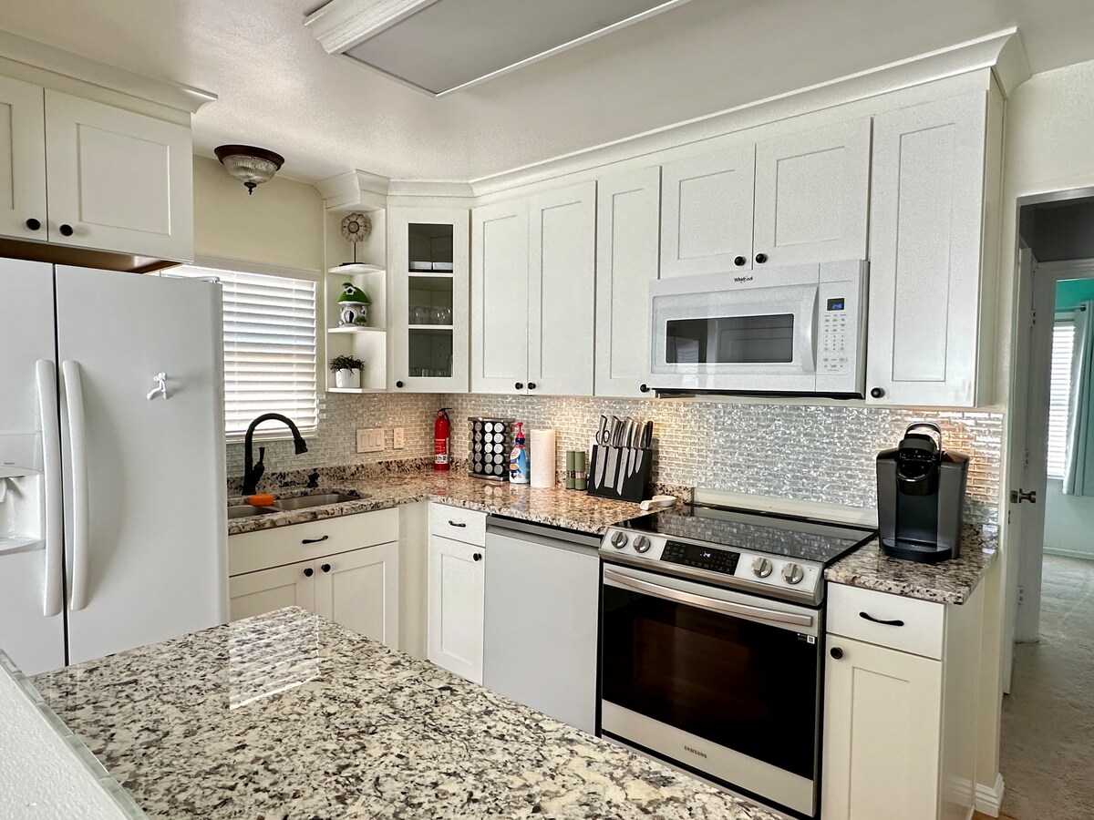 A well-equipped kitchen features modern appliances, including a stainless steel stove and microwave. White cabinetry contrasts with the granite countertops, and a decorative backsplash adds texture. A black coffee maker sits on the counter, and natural light filters through the window.