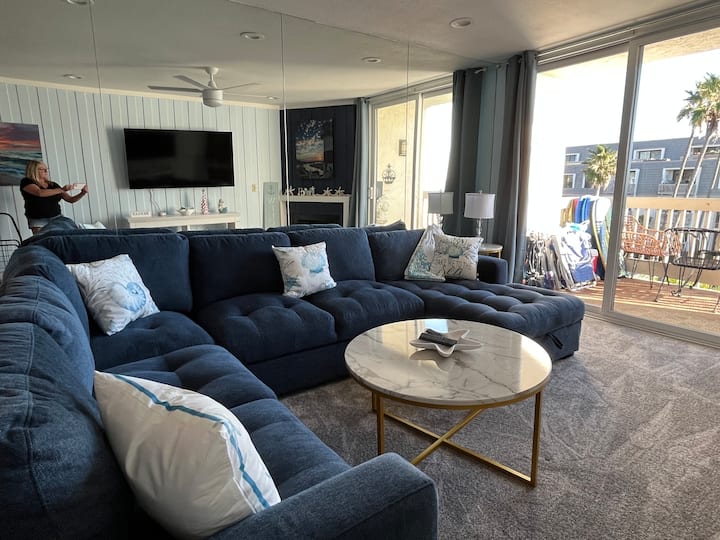 Sala con un gran sofá modular con cama extraíble y mucho espacio para que 6 personas se sienten cómodamente juntas a ver la televisión