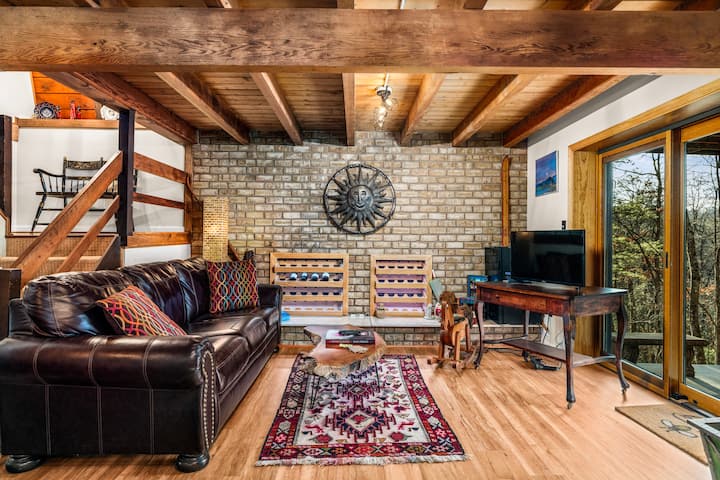 Acogedora sala de estar rústica con vigas de madera expuestas, pared decorativa de ladrillo, cómodos asientos de cuero y luz natural