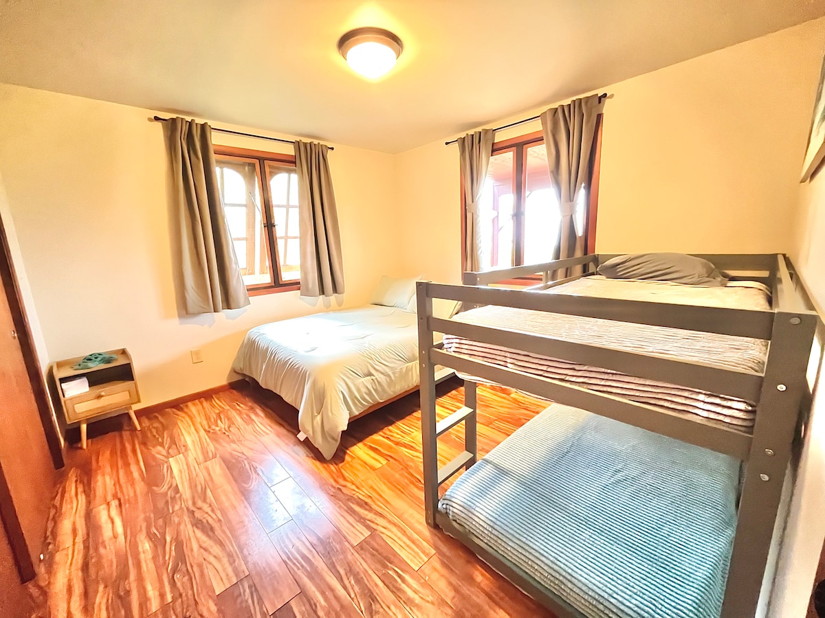 Bedroom features a queen bed and a twin bunk bed.  The windows have views of the ocean and the surrounding Hawaiian country.