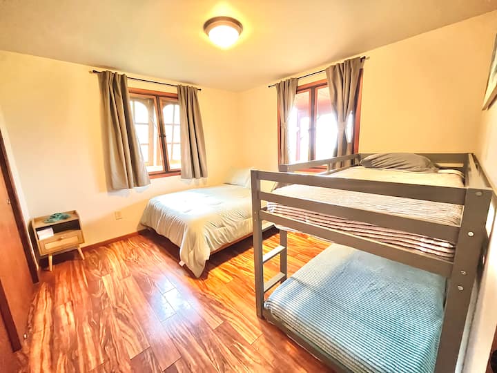 Bedroom features a queen bed and a twin bunk bed.  The windows have views of the ocean and the surrounding Hawaiian country.