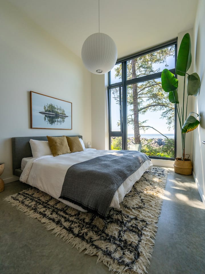 The master bedroom—featuring a king bed, luxe Brooklinen bedding, local art, and expansive ocean views for a restful retreat