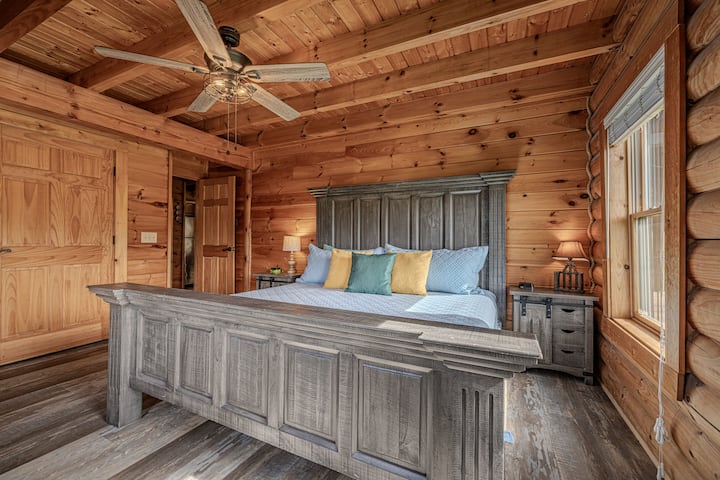 Suite confortable dans une cabane en rondins avec lit King Size, poutres, ventilateur au plafond et un charme ensoleillé.