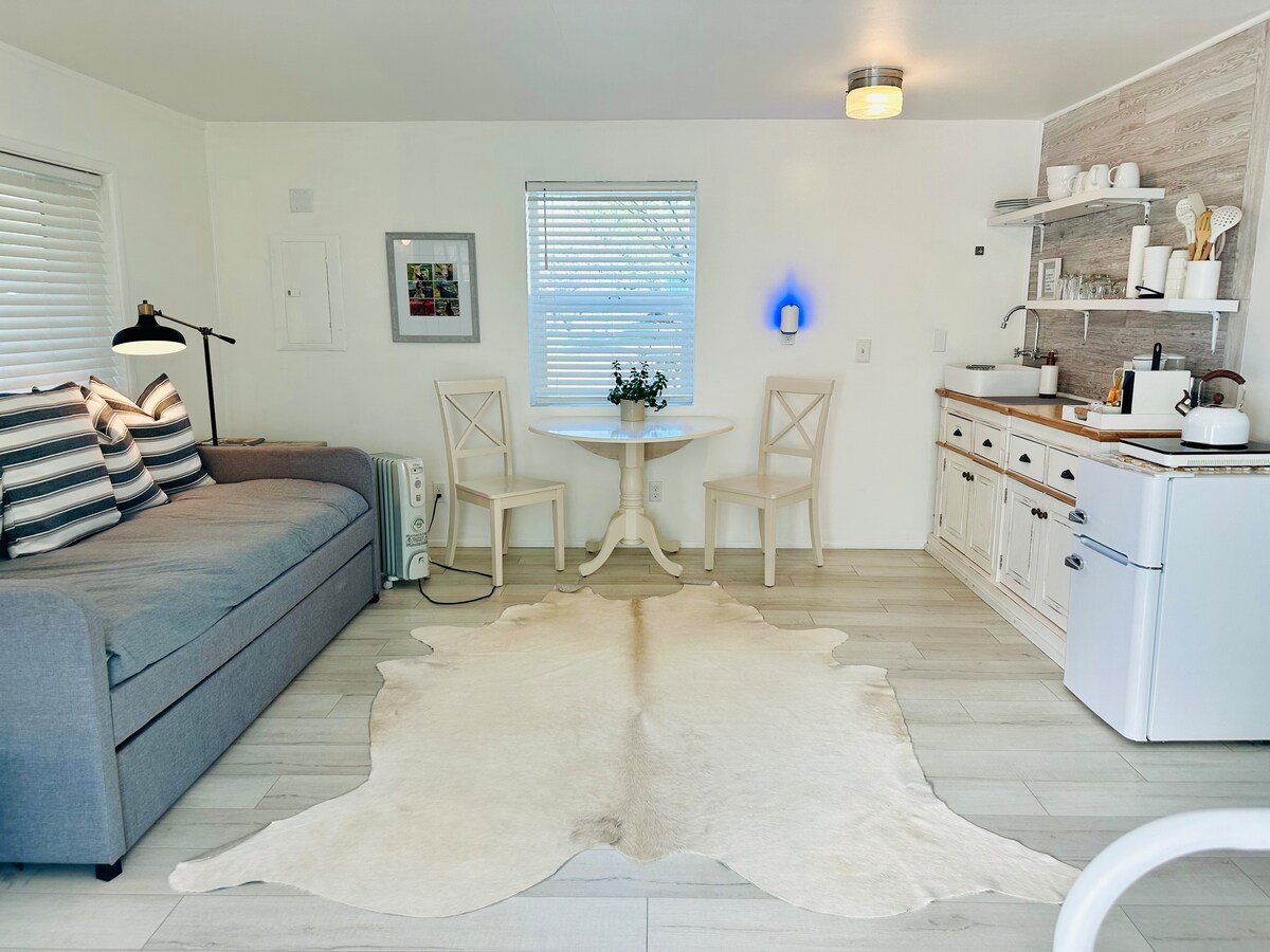 这是一间单间小屋，一端有一张标准双人床，另一端有一张带脚轮的沙发，墙边有一个小厨房。