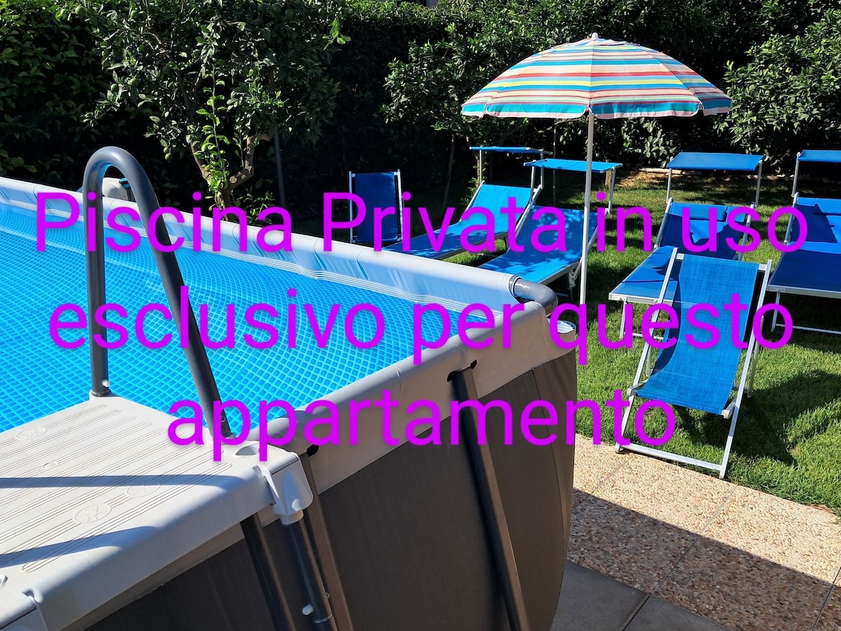 A private above-ground pool is prominently featured in the image, surrounded by well-maintained grass. Nearby, vibrant loungers and a colorful umbrella provide shaded seating. The pool area is designed for exclusive use by the apartment's guests, creating a relaxing outdoor space.