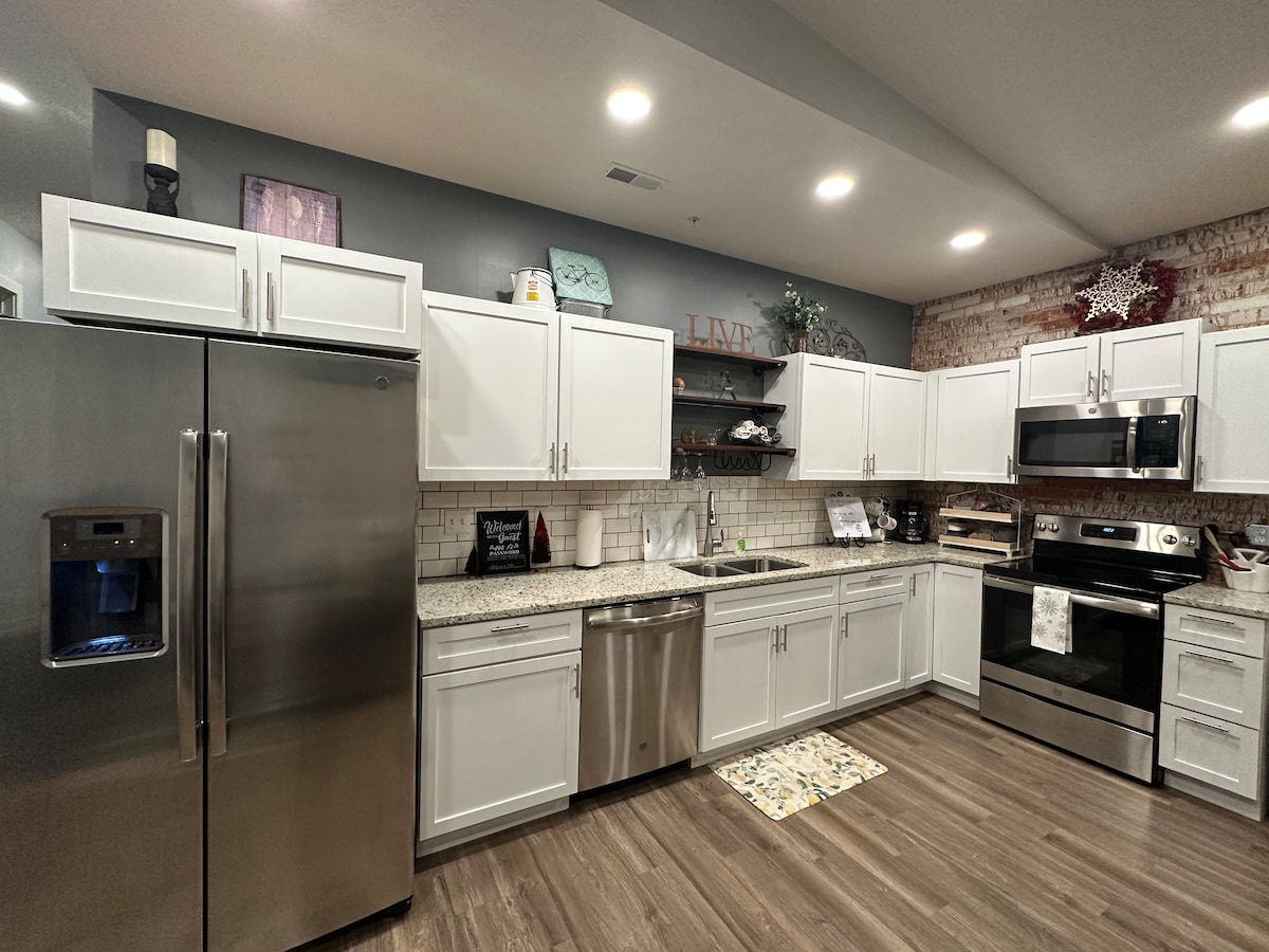 The kitchen features modern stainless steel appliances, including a refrigerator and oven. White cabinetry provides ample storage, complemented by granite countertops. A subtle tile backsplash adds texture, while a stylish rug lies on the wood-look vinyl plank flooring.