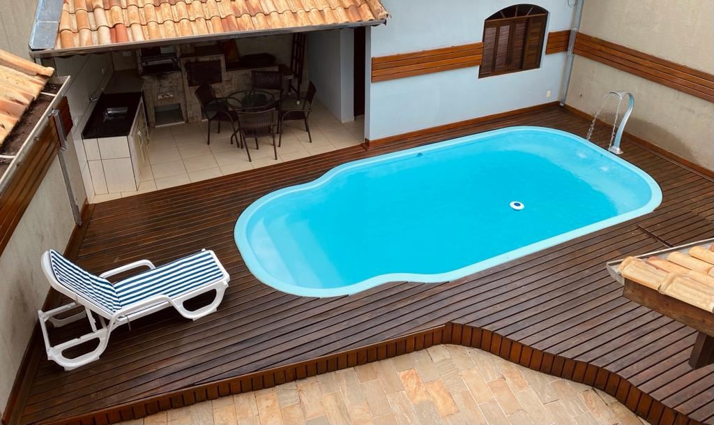 A private swimming pool is surrounded by a wooden deck, with a lounge chair positioned nearby for relaxation. The pool features a clean blue surface, and an outdoor dining area with a round table is visible under a covered patio.