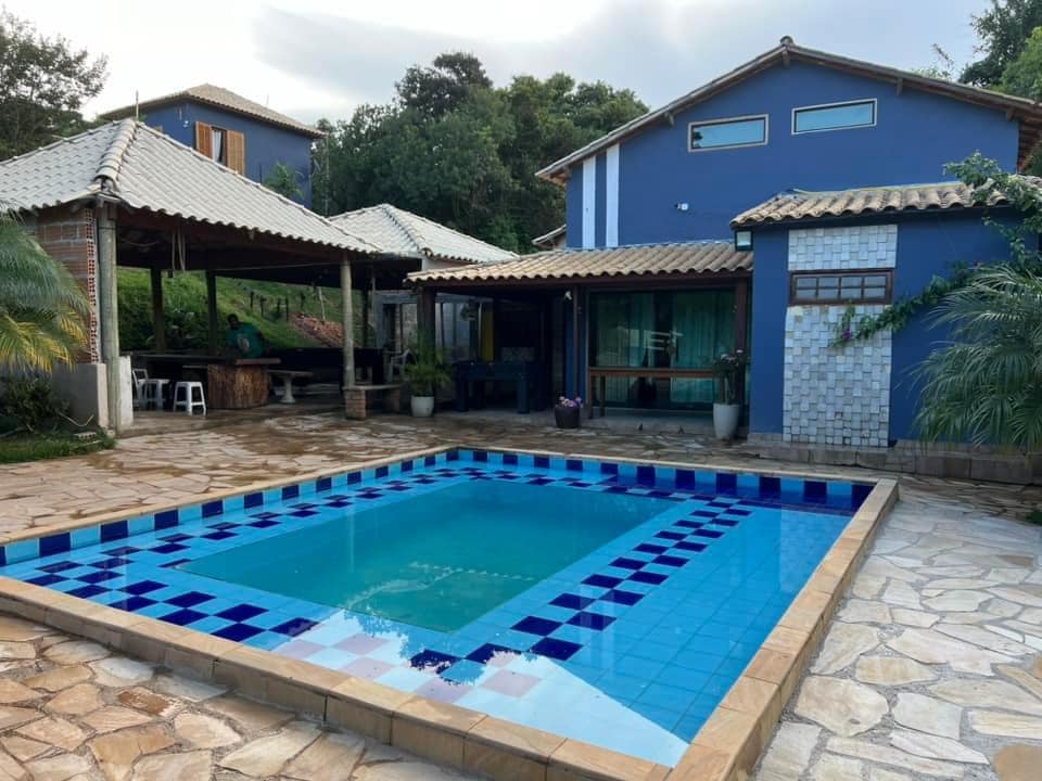 A picturesque outdoor area features a tiled swimming pool with vibrant blue accents. Surrounding the pool, a stone patio provides ample space for relaxation. A covered patio area is visible in the background, offering comfortable seating and views of the lush greenery.