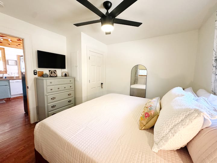This king bedroom is just off the kitchen and features a smart TV, plenty of drawers, a closet with extra bedding and a box fan, a diffuser, and a portable workstation desk.