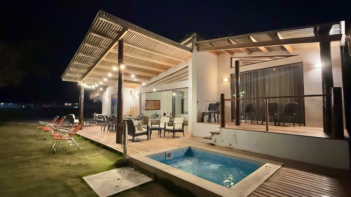 The home exterior is illuminated at night, featuring a covered terrace with outdoor seating. A small pool is set beside the terrace, while lounge chairs are positioned in the yard, creating a relaxing outdoor environment. The ambiance is calm and welcoming.