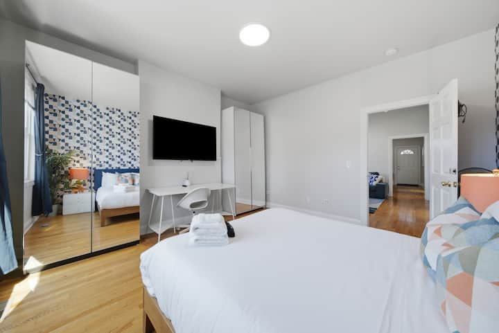 Chambre principale au premier étage avec un lit Queen Size, une télévision connectée, un bureau dédié, une armoire spacieuse et une lumière naturelle abondante. Un lieu de repos confortable pour les voyageurs d'affaires comme pour les vacanciers.