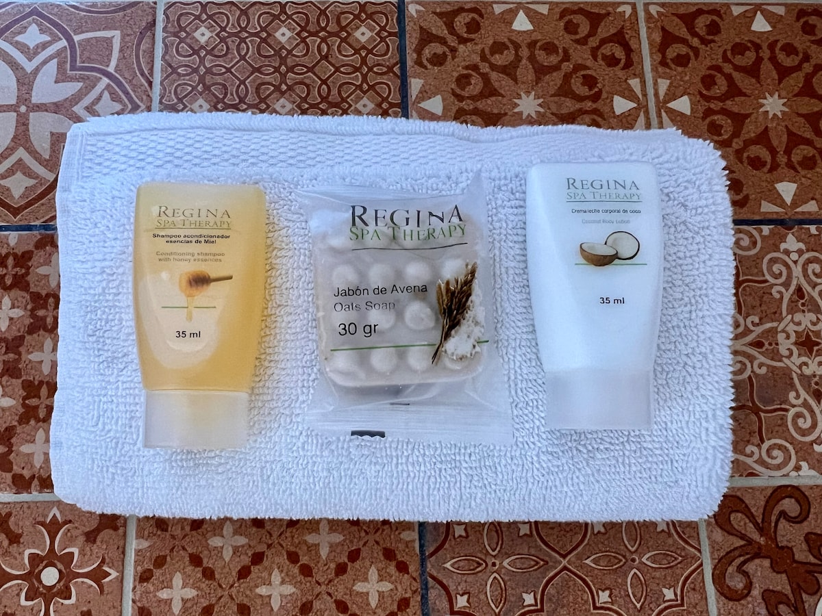 A plush white towel is neatly folded, providing a backdrop for three spa therapy products. The left contains liquid soap, the center showcases a soap package, and the right features a moisturizing cream, all labeled with 'Regina Spa Therapy'.