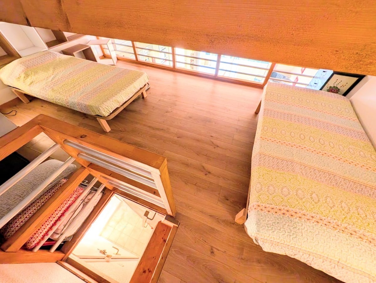 SPÁLŇA 2 v nízkom medziposchodí s výhľadom na obývaciu izbu s dvoma lôžkami (90 x 190), prikrývkou a vankúšmi.