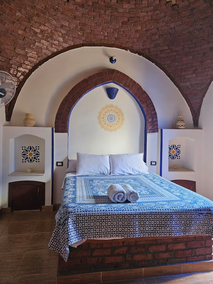 Dormitorio con cama tamaño queen y balcón frente a la villa. El dormitorio tiene un tocador y un armario de palmeras hecho a mano con estante y estantes para colgar ropa y guardar artículos personales.
