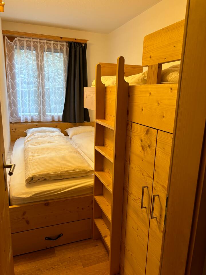 Малка, уютна детска стая с вградено двойно легло, направено от дърводелеца, гардероб и единично двуетажно легло.