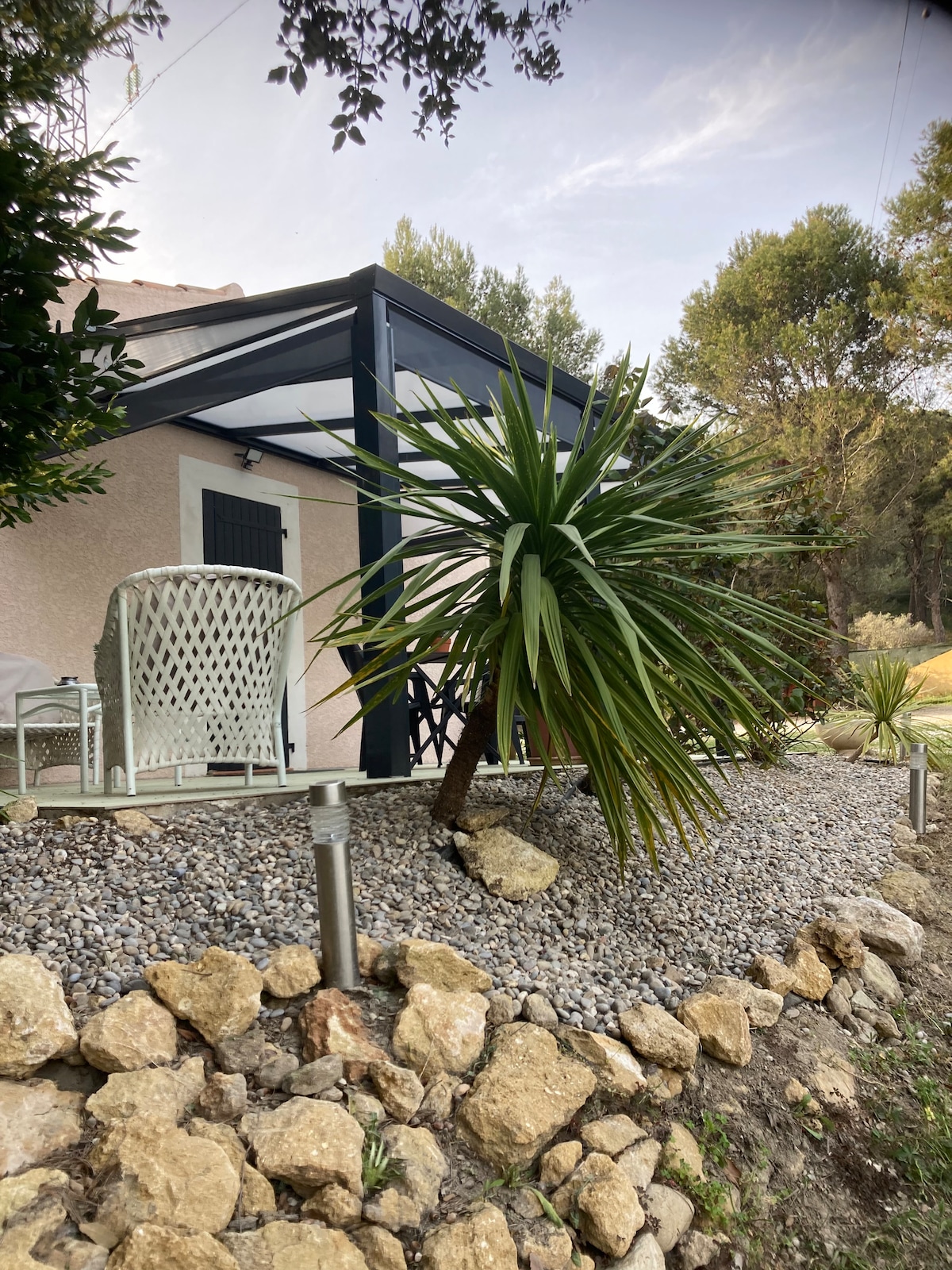 An outdoor area is depicted featuring a private terrace. Comfortable seating is available beside a variety of plants, including a tall yucca tree. The space is surrounded by a decorative gravel garden and small rocks, creating a natural yet structured environment.