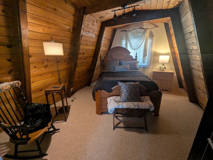 The upstairs queen bedroom — warm wood walls, soft bedding, and a quiet tucked-away feeling that makes mornings hard to leave.