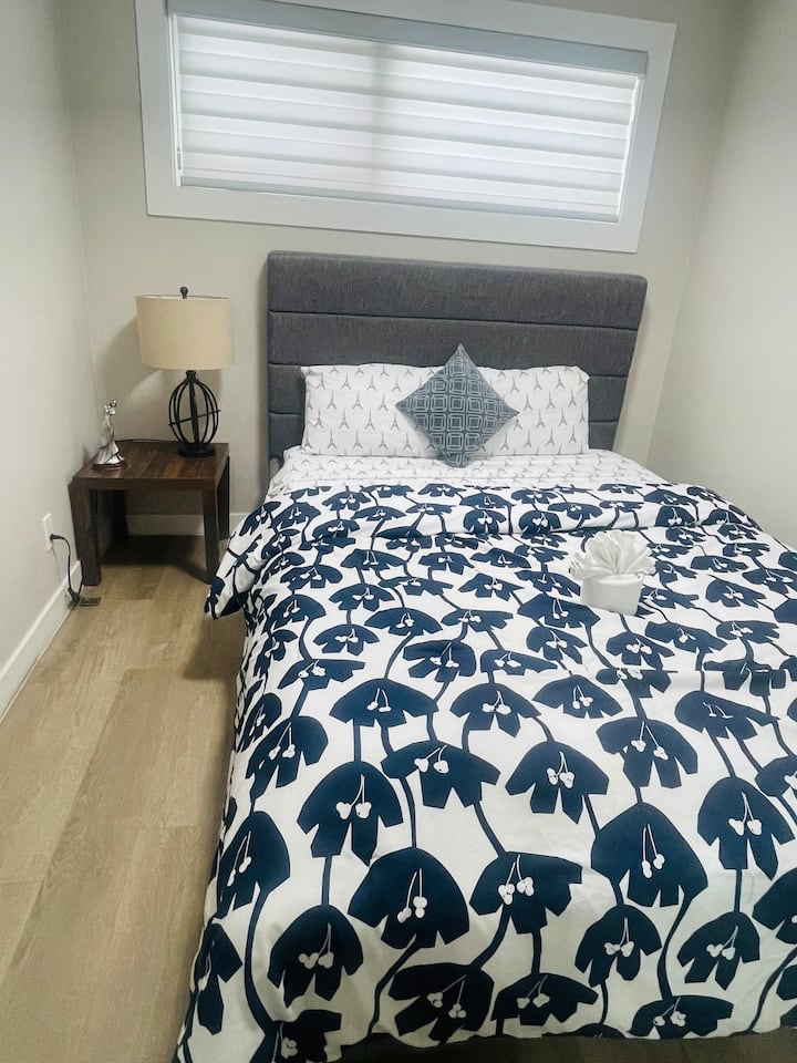 Una lujosa cama de matrimonio con una sofisticada cabecera gris acolchada. Está decorada con sábanas de primera calidad en azul marino y con estampado floral en blanco, lo que le confiere un aspecto fresco, limpio y de diseño.