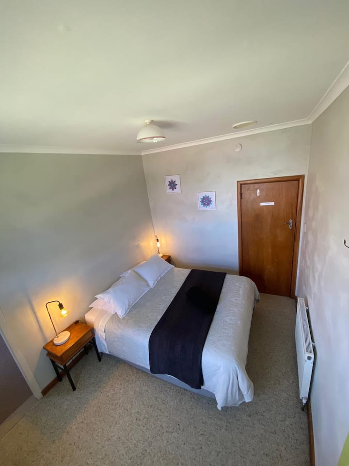 Dormitorio 2 con cama tamaño queen adyacente a la sala de estar/cocina pequeña con calefacción por radiador.