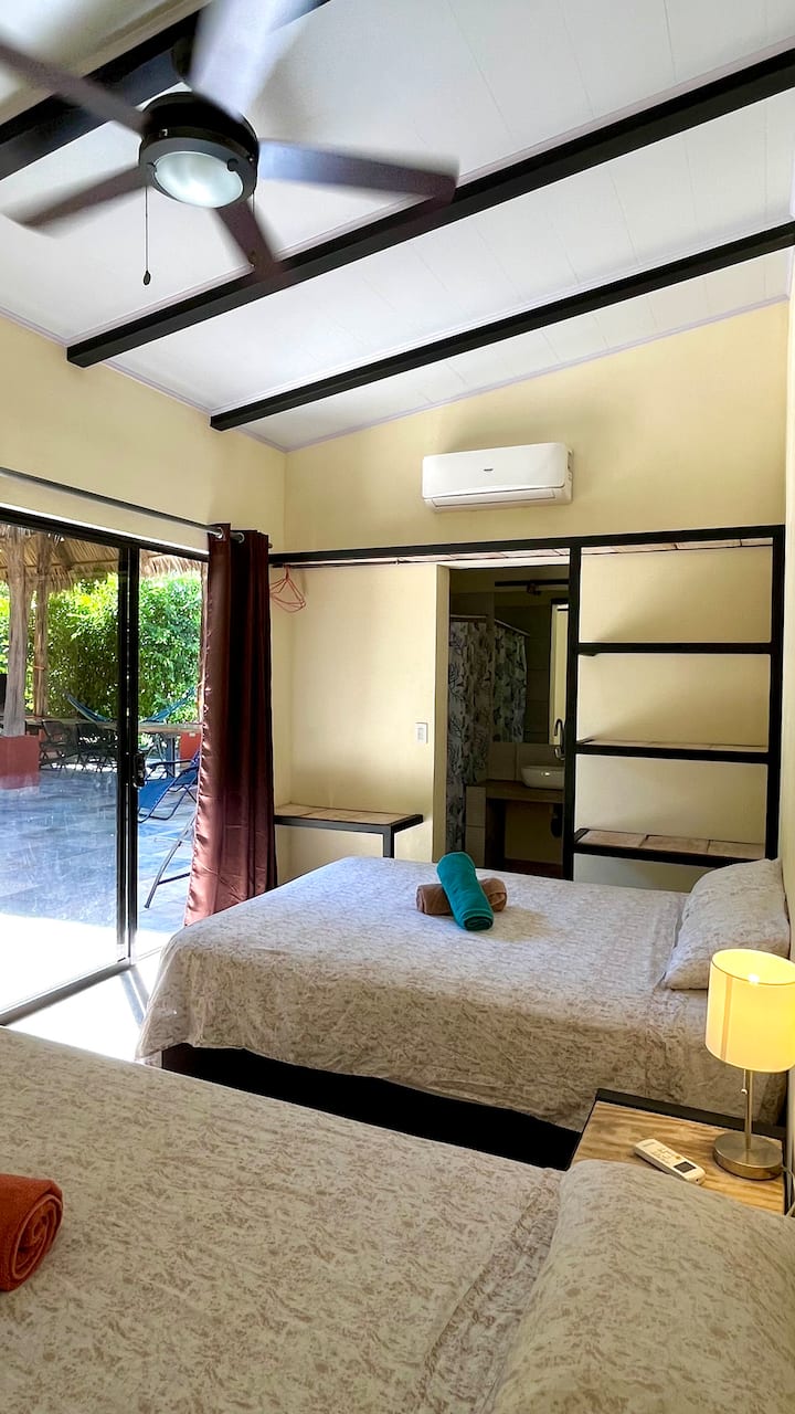 Chambre confortable équipée de deux lits doubles, avec salle de bain privée, climatisation et vue sur la piscine.