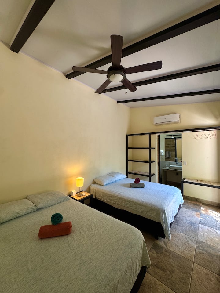 Chambre confortable équipée de deux lits doubles, avec salle de bain privée, climatisation et vue sur la piscine.