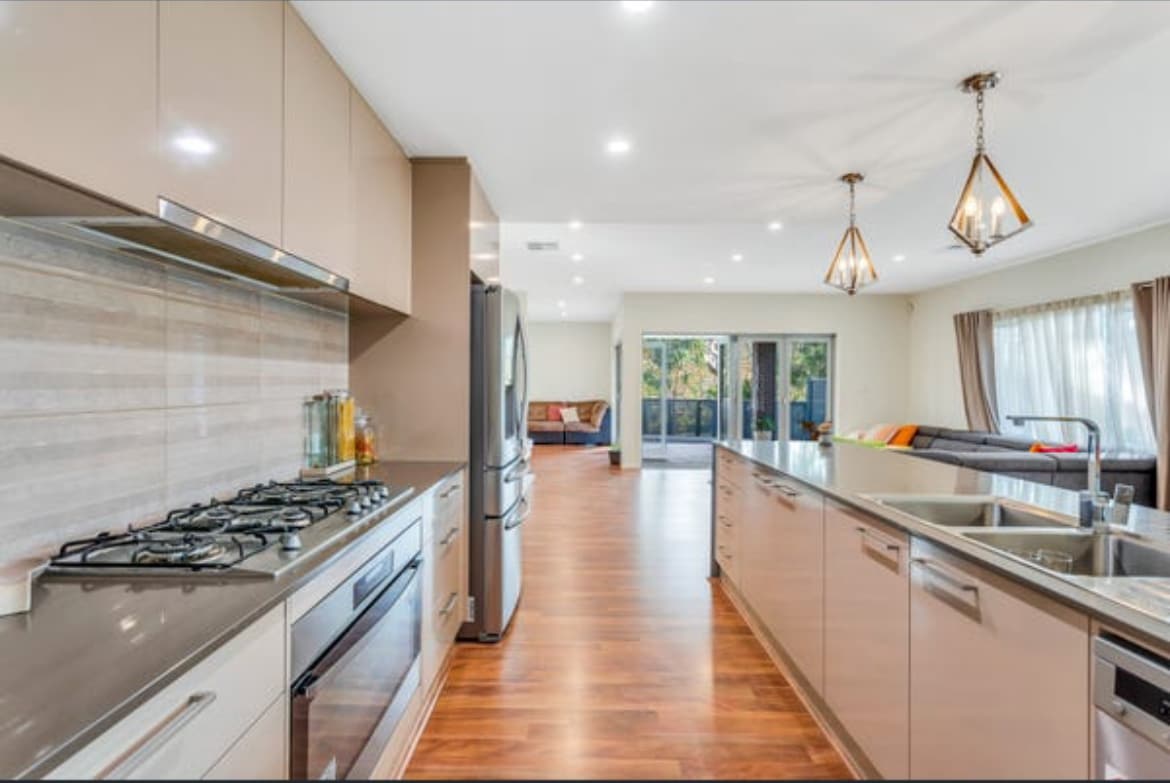 The modern kitchen is equipped with stainless steel appliances, featuring a gas stove and a spacious counter. Natural light flows through large windows, illuminating the open layout that connects to the living area. Pendant lights enhance the sleek design of the space.