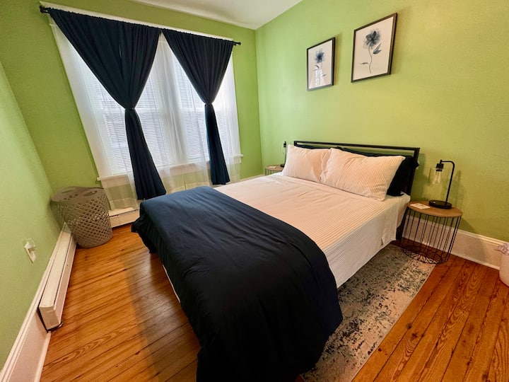 تحتوي غرفة النوم الخضراء على صندوق ورف أمتعة ومصابيح بجوار السرير وستائر داكنة للغرفة ومروحة سقف لمزيد من الراحة. 