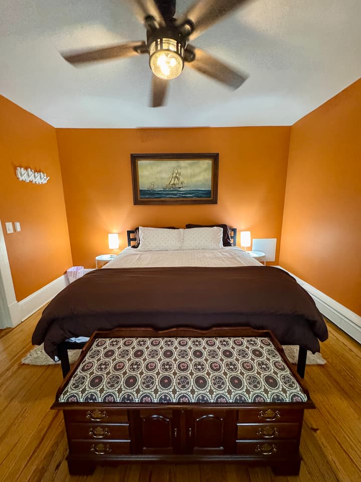 تحتوي غرفة النوم البرتقالية على صندوق جلوس ورف أمتعة ومصابيح بجوار السرير وستائر داكنة للغرفة ومروحة سقف لمزيد من الراحة. 