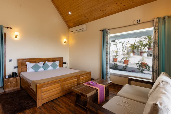 Charming chalet bedroom with vaulted pine ceiling, solid wood king bed, teal cushions & AC. Warm wall sconces create a cozy mountain lodge feel.