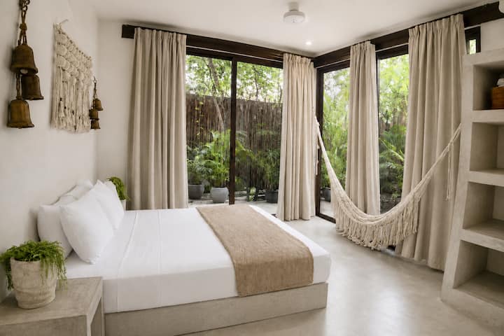 Dormitorio tropical luminoso con hamaca y exuberantes vistas al jardín