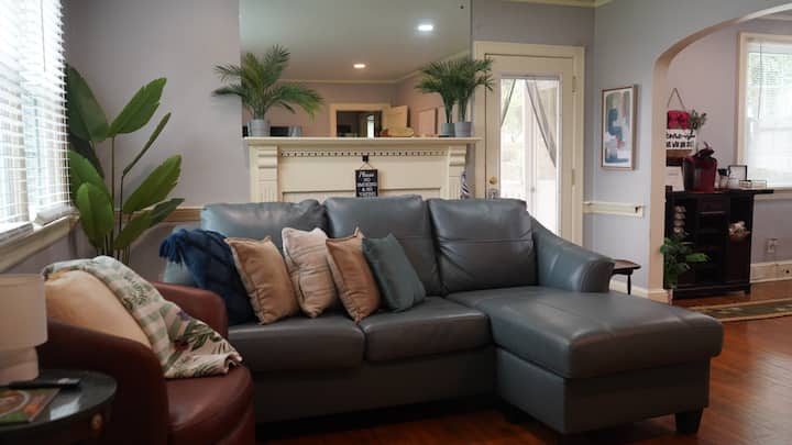 Влезната врата се отвора кон добро осветлена дневна соба со топла, природна сончева светлина. Кожно седење, удобен кауч во стил на шезлонг и стол со акцент. Голем паметен телевизор за емитување емисии, вести, спорт или филмови. Пристап до страничен трем, ходник или трпезарија.