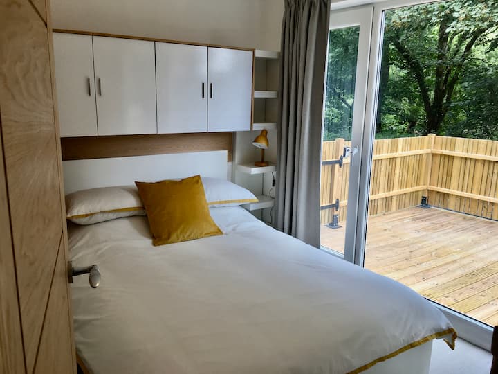 The comfortable main bedroom looks out onto a private raised decked area through full-height glazed windows. The bedroom has a double bed, plenty of built in storage and a USB charging plug. All bedding is included in your stay.