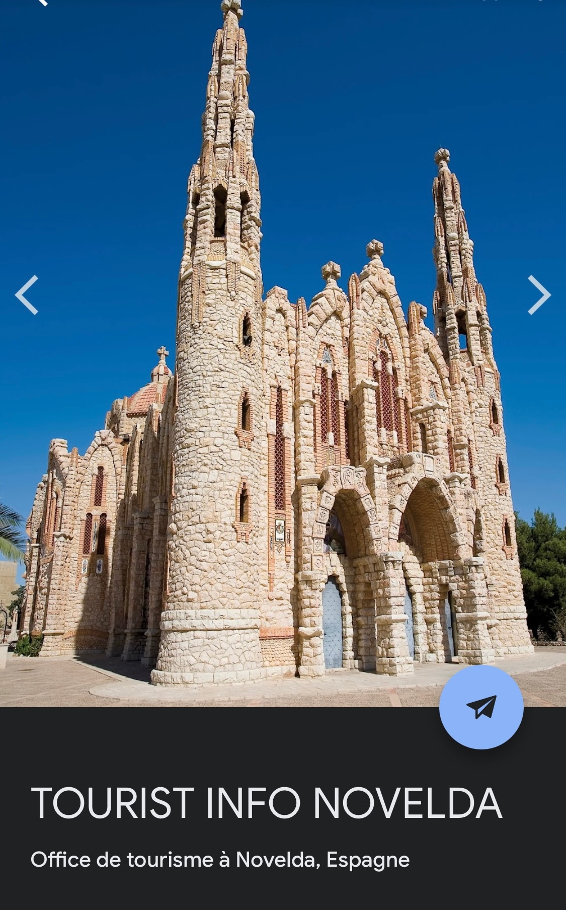 A stone building is depicted with intricate architectural details, featuring tall spires and arched windows. The structure is surrounded by clear blue skies and sits on a broad pathway. The texture of the stone and the design elements convey a historical significance.