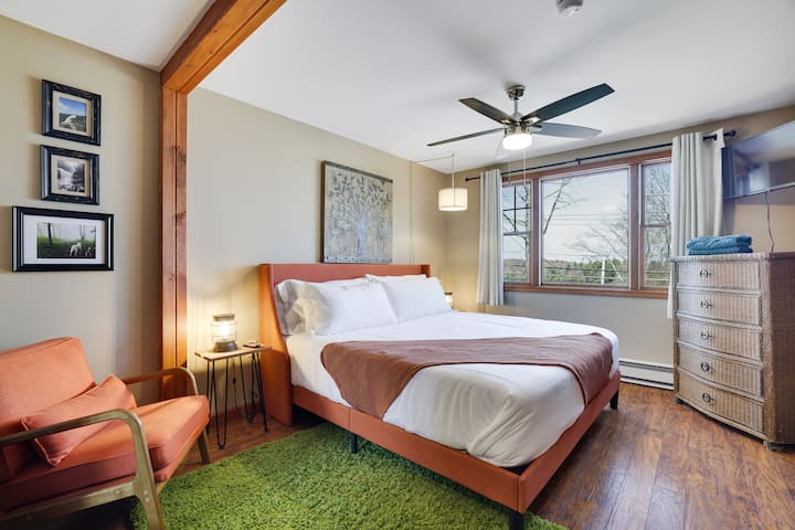 Bright king bedroom en suite with lake views, TV, ceiling fan & real wood floors