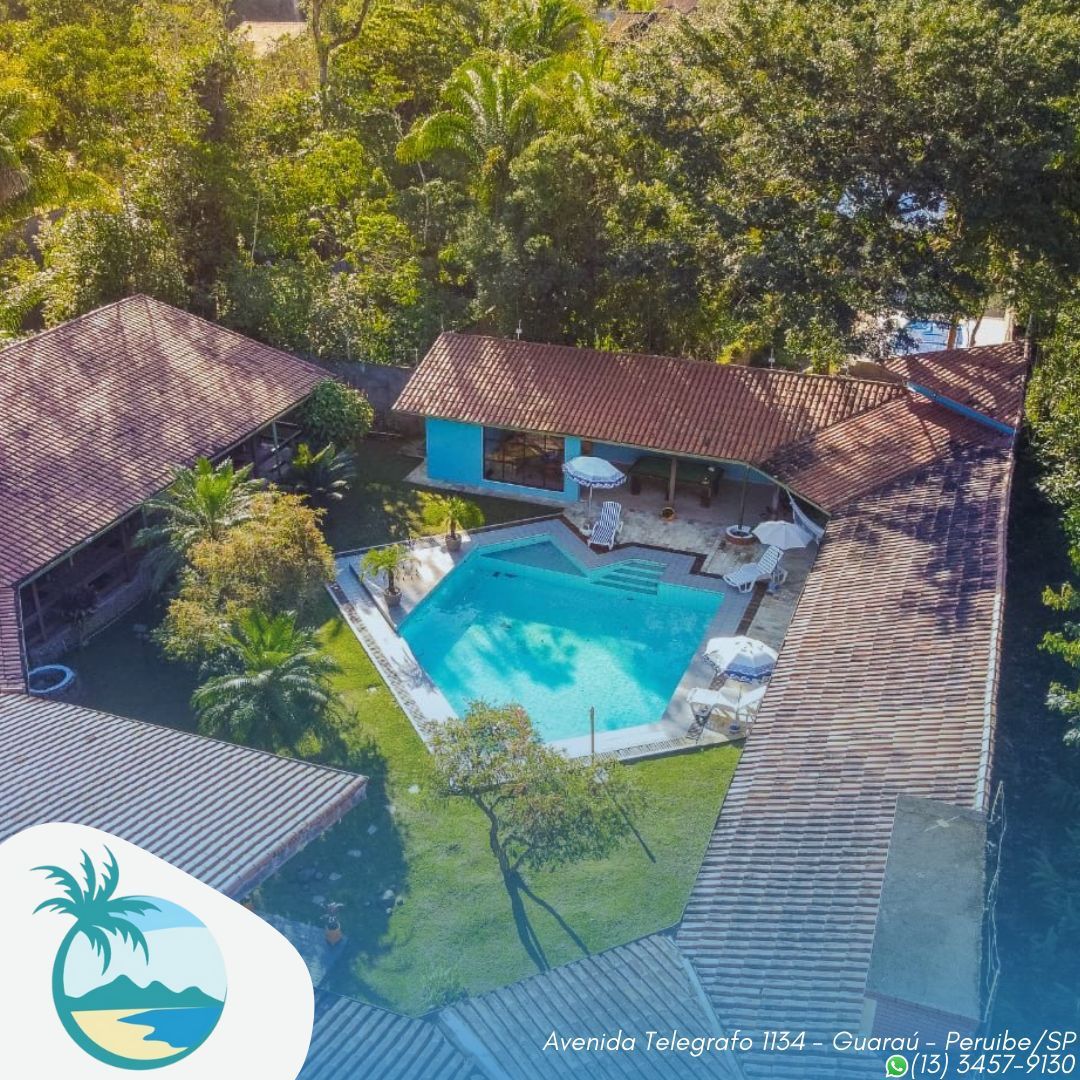 An aerial view of a property featuring a central swimming pool surrounded by a lush garden. The pool area is equipped with white loungers and parasols. The buildings have terracotta roofs and are positioned in a circular layout, emphasizing a communal outdoor space.