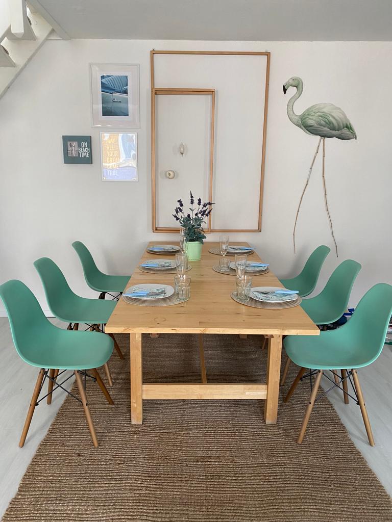 A dining area is presented with a wooden table surrounded by six mint green chairs. The table is set with plates and glasses, enhancing a functional yet welcoming arrangement. A large wall art piece featuring a flamingo adds a decorative touch above the table.
