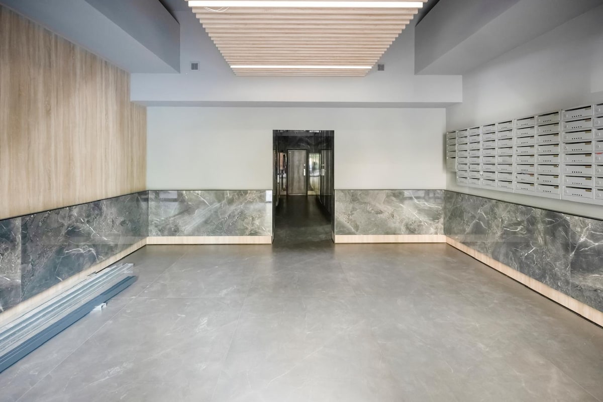 A spacious lobby area is depicted, featuring polished concrete floors and elegant marble wall panels. A dark entrance door leads to another space, while organized mailboxes are mounted on one side. Soft overhead lighting creates a welcoming environment.