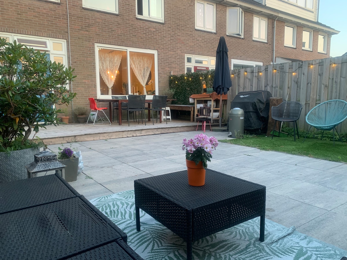 A patio area is featured, showcasing a black coffee table surrounded by comfortable seating. Potted plants add greenery to the space, while outdoor dining tables are visible in the background. Soft lighting creates a welcoming ambiance, enhancing the overall outdoor experience.