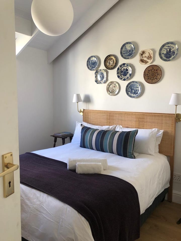 Chambre à coucher récemment construite à l'étage avec un lit queen size avec tête de lit en rotin, de hauts plafonds et de la lumière naturelle. Décoré avec soin avec des assiettes anciennes et du linge de qualité pour un séjour reposant et élégant