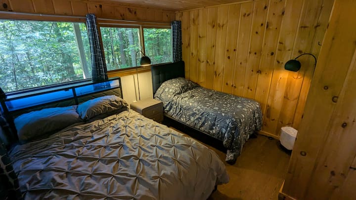 This bedroom has wrap-around windows with a queen bed, a twin/single bed, a closet, and a dresser.