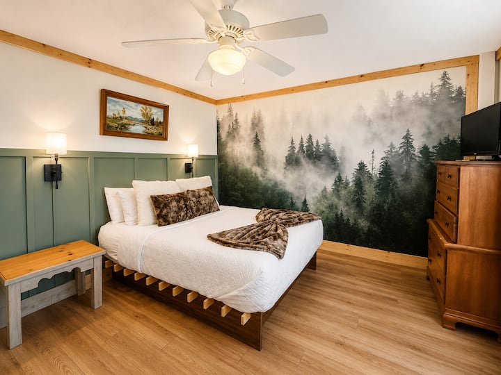 Unwind in this cozy mountain-inspired bedroom, complete with a beautiful forest mural, warm wood accents, and soft, inviting bedding.