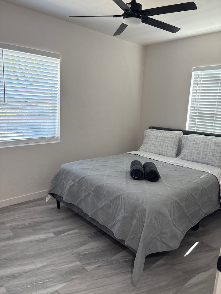 חדר שינה נעים עם מאוורר תקרה, שהוא מושלם לשמירה על קור רוח. יש שני חלונות עם תריסים לבנים, המאפשרים לאור טבעי לסנן פנימה תוך שמירה על פרטיות. חדר אסתטי מודרני ונקי.