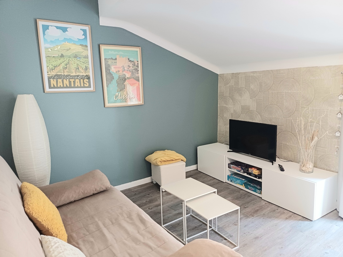 A cozy living area features a light brown sofa and two white coffee tables. Framed artwork illuminates the walls, complemented by a contemporary television on a sleek white media console. A textured wallpaper adds depth, while a soft throw is casually placed over the sofa.
