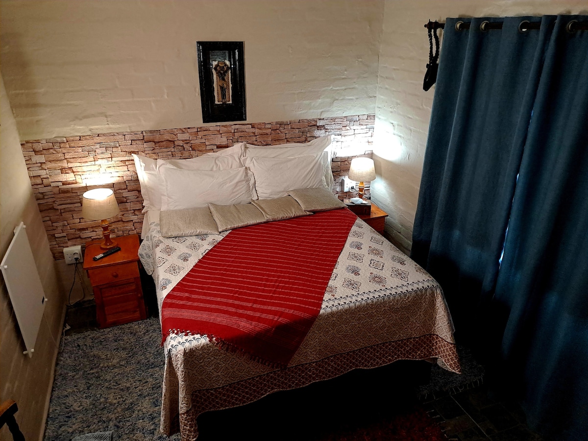 A cozy bedroom features a spacious bed adorned with a patterned blanket. Two bedside tables with lamps provide soft lighting. A textured wall behind the bed enhances the room's aesthetic. Dark blue curtains frame a window, allowing for natural light.