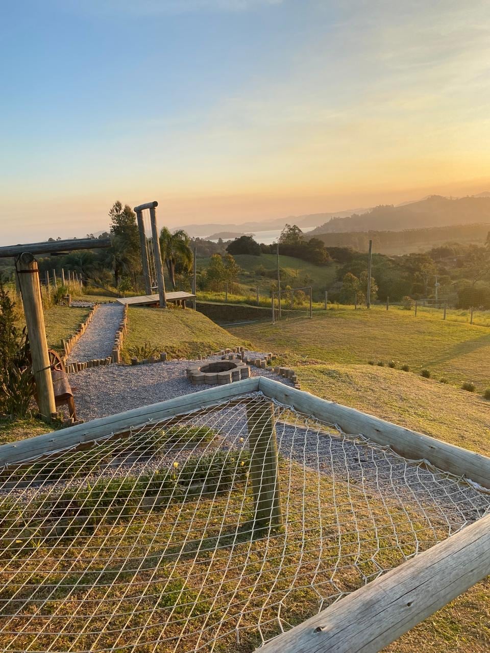 A wide-open landscape captures the peaceful setting of the countryside, with rolling hills and a distant view of water reflecting the sunset. A walking path is framed by wooden fencing, inviting guests to explore the natural beauty of the area.