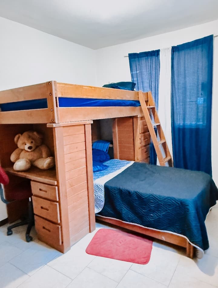ห้องพัก 1 ที่ชั้นล่าง เครื่องปรับอากาศเย็น/ร้อน พร้อมเตียงสองชั้นขนาดเดี่ยว 2 เตียง ที่นอนเสริม พื้นที่ทำงานขนาดเล็กพร้อมโต๊ะและเก้าอี้หมุน ลิ้นชักสำหรับเก็บเสื้อผ้า สมาร์ททีวี วิวถนนและโรงจอดรถ