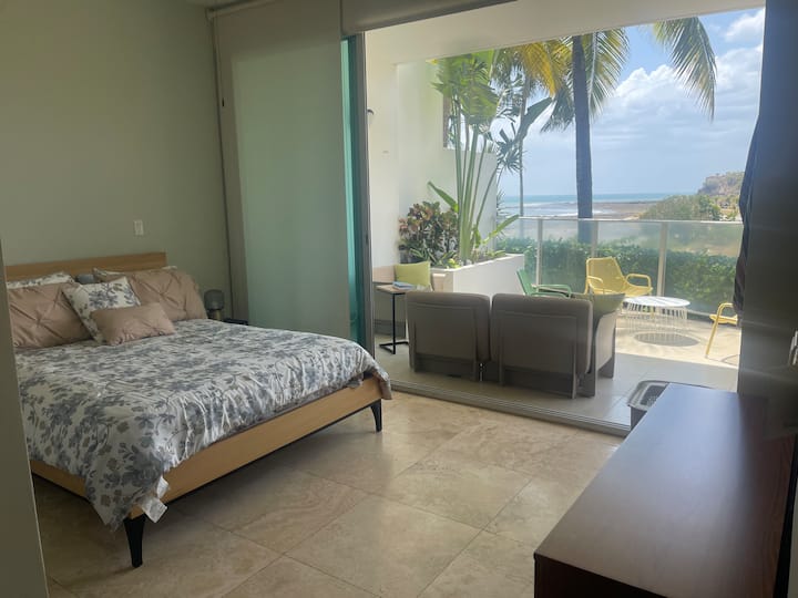 Veľká manželská posteľ a výhľad na exteriér a vonkajší nábytok.
Upozorňujeme, že obe okenné tabule sú otvorené.
Veľké okenné tabule od podlahy až po strop poskytujú dostatok prirodzeného osvetlenia a výhľad na vonkajšiu zeleň.