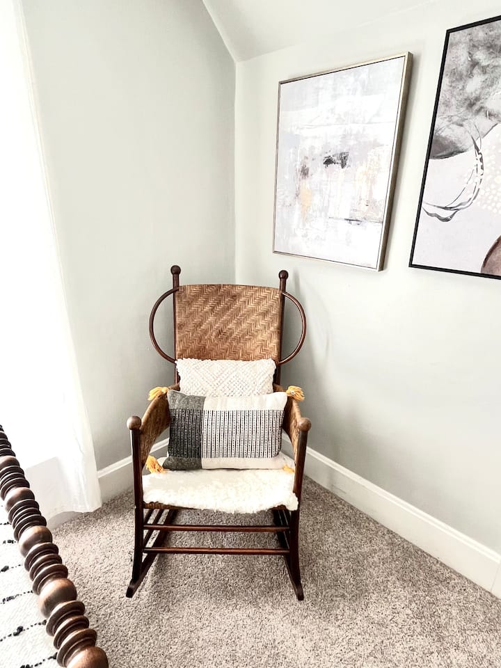 Thurje antike dhe karrige lëkundëse druri në cepin e mbushur me diell të dhomës së gjumit private.